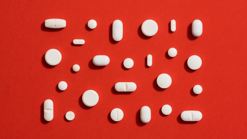 Assorted white pills arranged neatly against solid red background