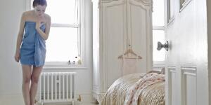 Young Caucasian woman in apartment bedroom weighing herself on scale