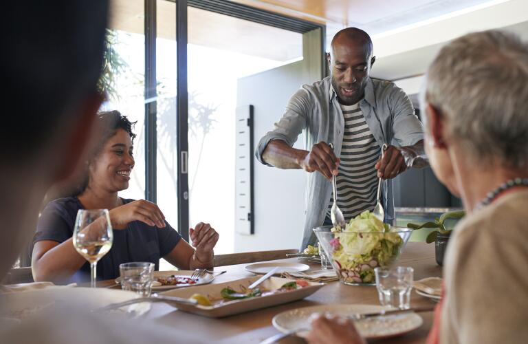 Middle age African American man tossing salad on dinner table for family meal
