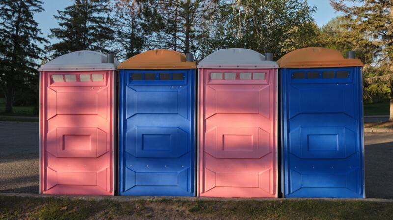 Four port-a-potties in a wooded setting