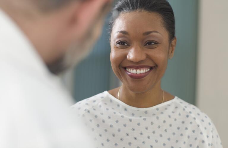 Close-up of African American female patient in hospital gown smiling at doctor
