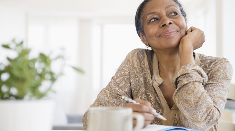 senior woman sitting at table thinking and writing