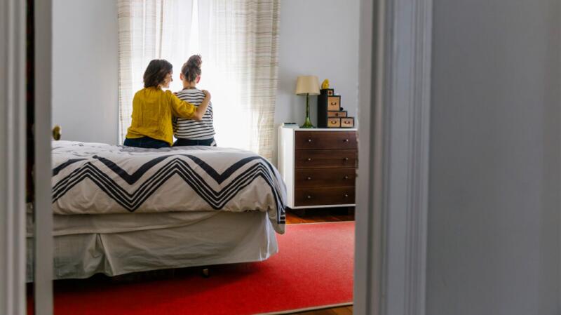 Two women sitting on a bed hugging
