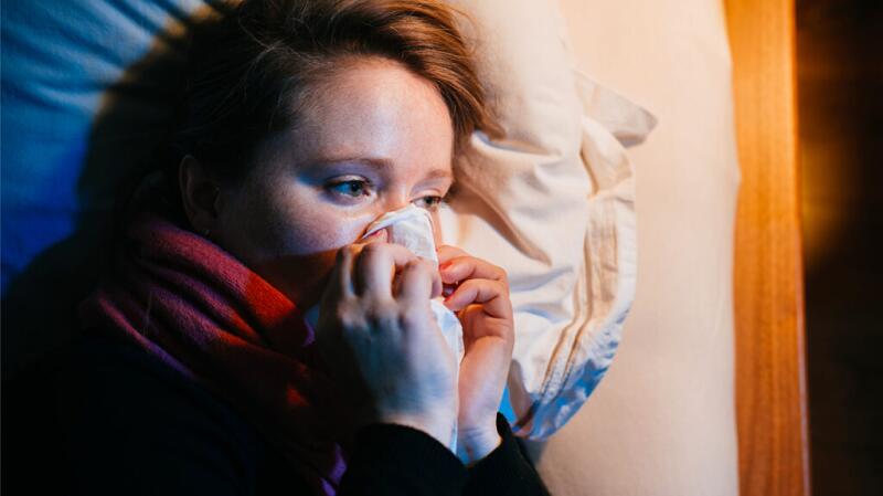 a person is lying in bed blowing their nose