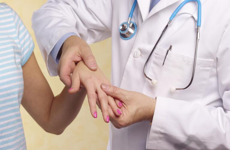Close-up of rheumatologist or joint doctor examining left hand of young female patient