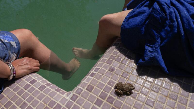 Two people sit on the side of a pool, dipping their legs in the water.