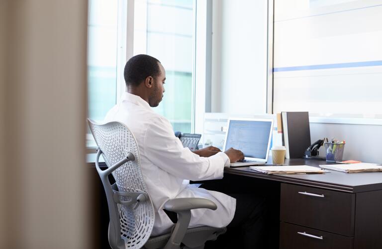 African American male doctor typing on laptop at desk in office
