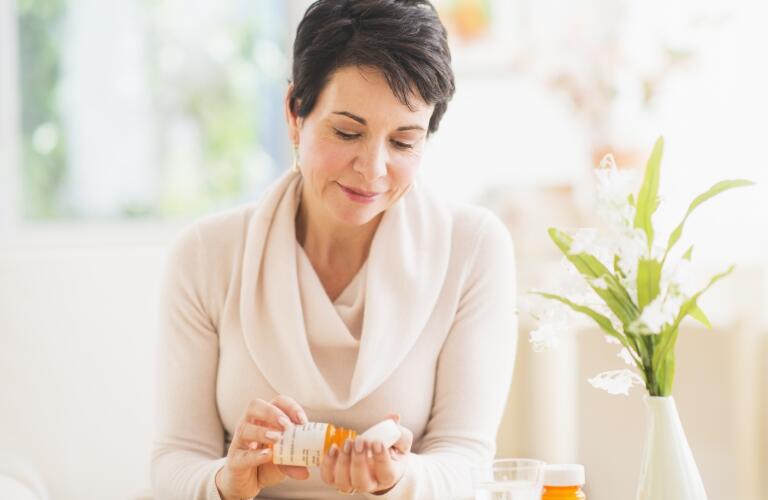 Middle aged Caucasian woman taking pill from prescription bottle