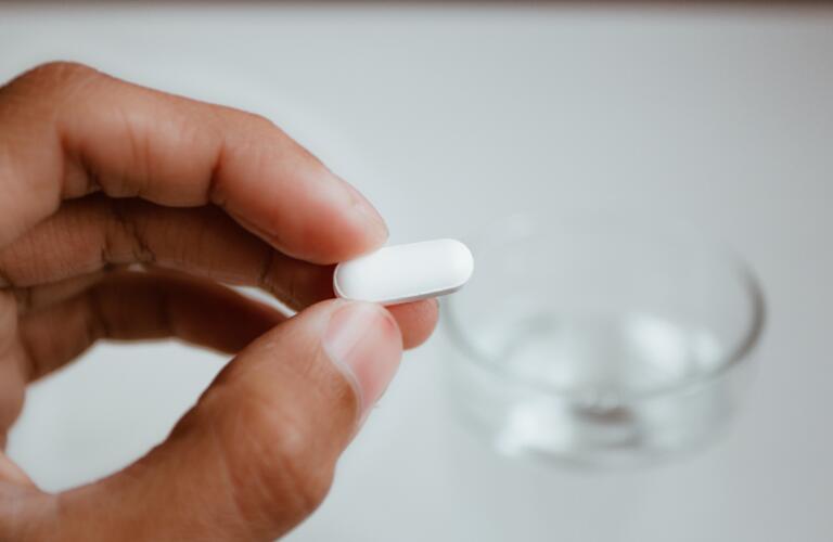 hand holding pill over glass of water