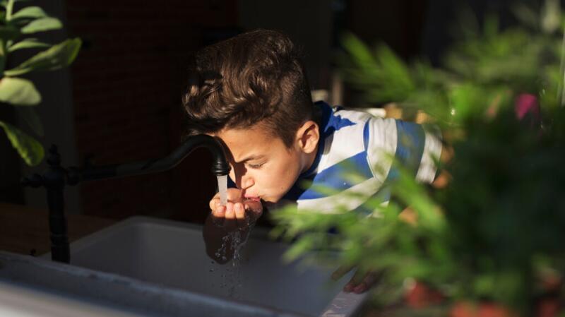 A child drinking water from his hand under a faucet