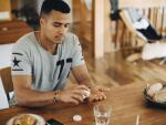 Young Hispanic man taking pill at kitchen table 