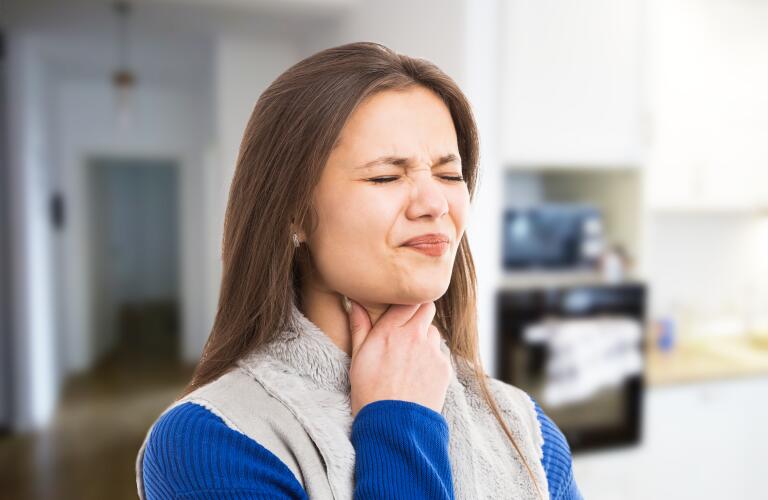 young woman with sore throat, squeezing eyes shut with painful swallowing