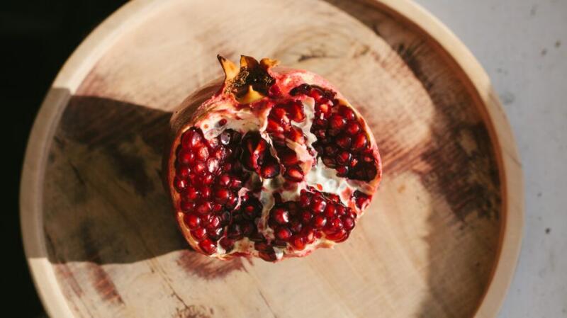 An open pomegranate rests on a round wooden plate, showing its seeds.
