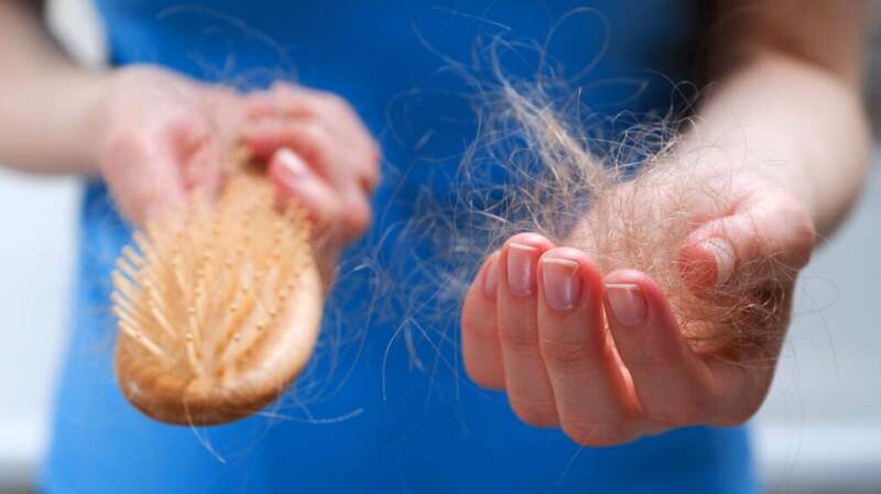 A woman holding loose hairs and a hair brush