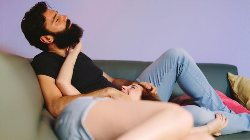 A man with thick hair and a beard sitting on a couch with a woman