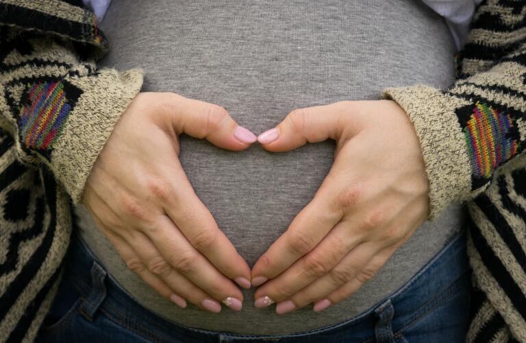 Woman holding pregnant belly with hands in shape of a heart