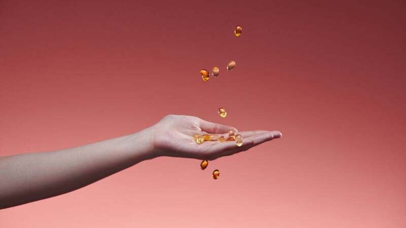 An outstretched hand catching fish oil capsules