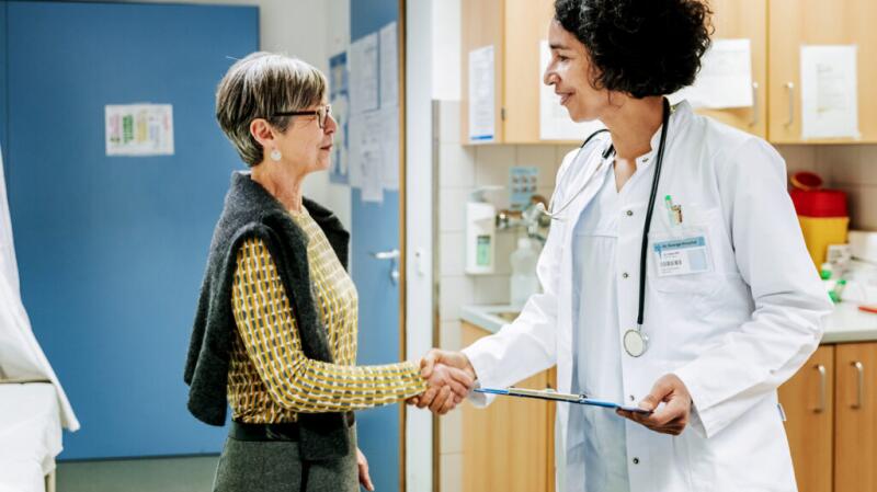 Female doctor shaking hand of female patient in medical office hallway
