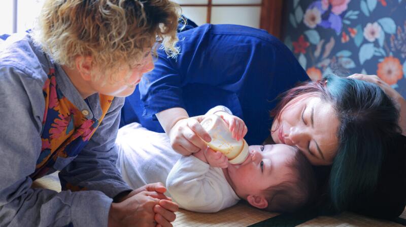 Female couple with newborn baby feeding with bottle on floor