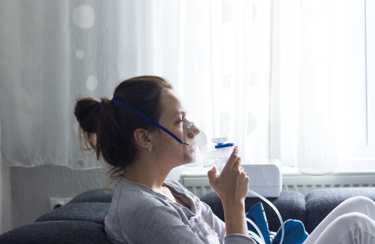 Young woman using asthma nebulizer on couch