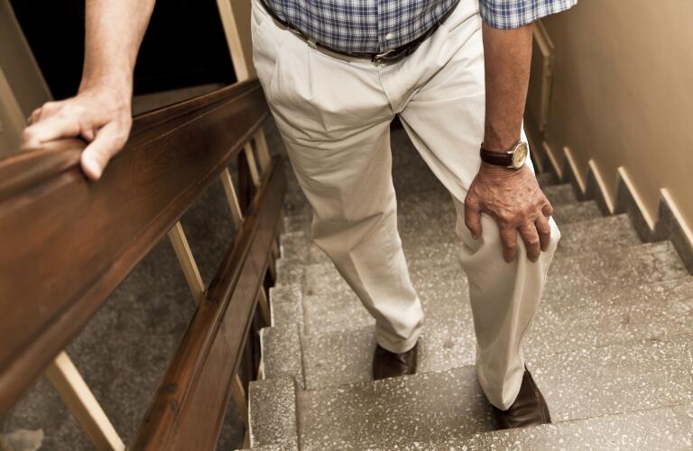 Unseen older man experience knee pain on stairs