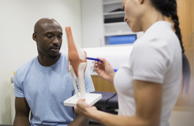 Young African American male patient look at knee model with Asian American female doctor or therapist