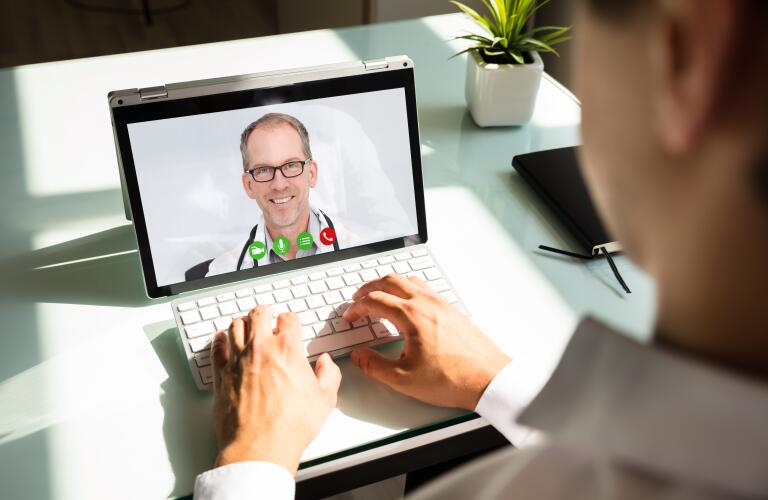 Unseen male patient talking to male Caucasian doctor via telemedicine on laptop video chat