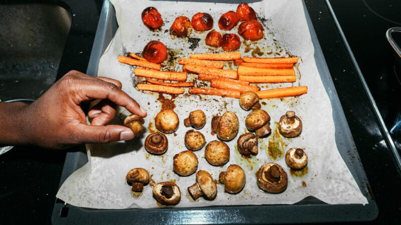 A person's hand picking up a mushroom from a pan full of vegetables