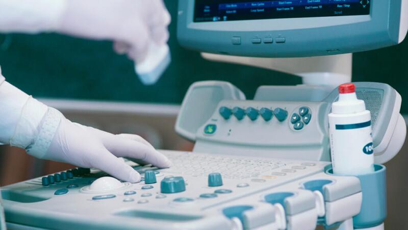 A closeup of a physician's hands touching an echocardiogram machine