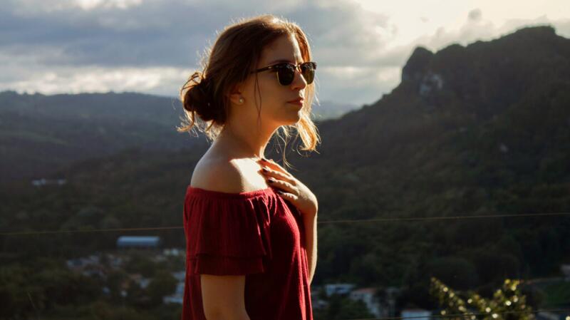 Woman stands outside, holding hand against upper chest and sternum