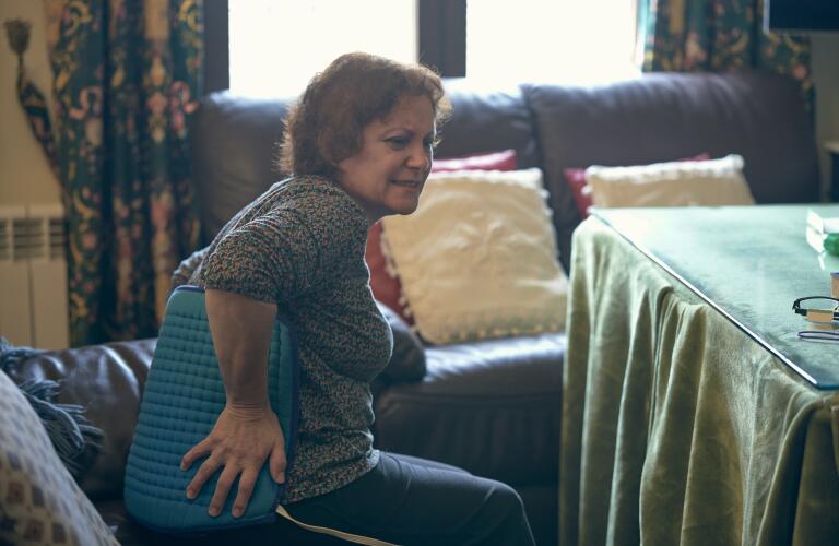 Older woman on couch with heating pad on back