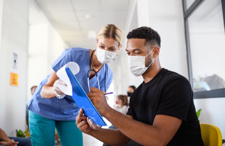 female nurse holding clipboard for male patient to sign a form, both wearing face masks; coronavirus, covid-19 and vaccination concept