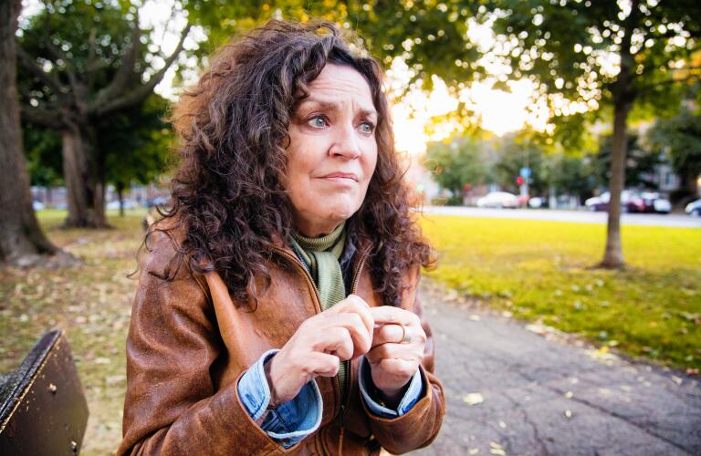 Anxious woman sitting on park bench looking nervous