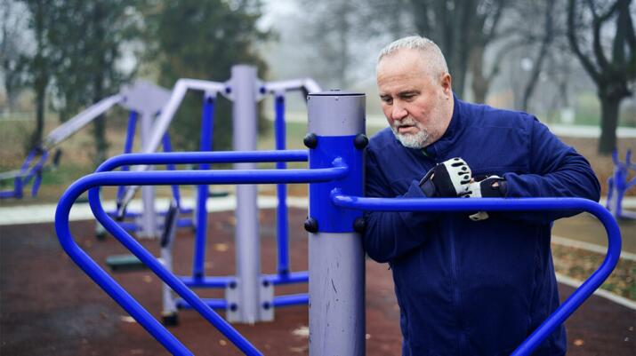 an older man is at an outdoor gym holding his chest