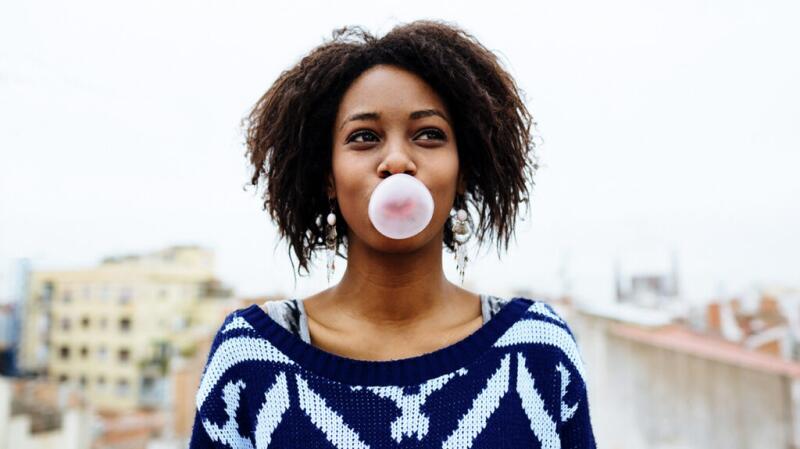 Woman standing outside blowing bubble with pink bubblegum