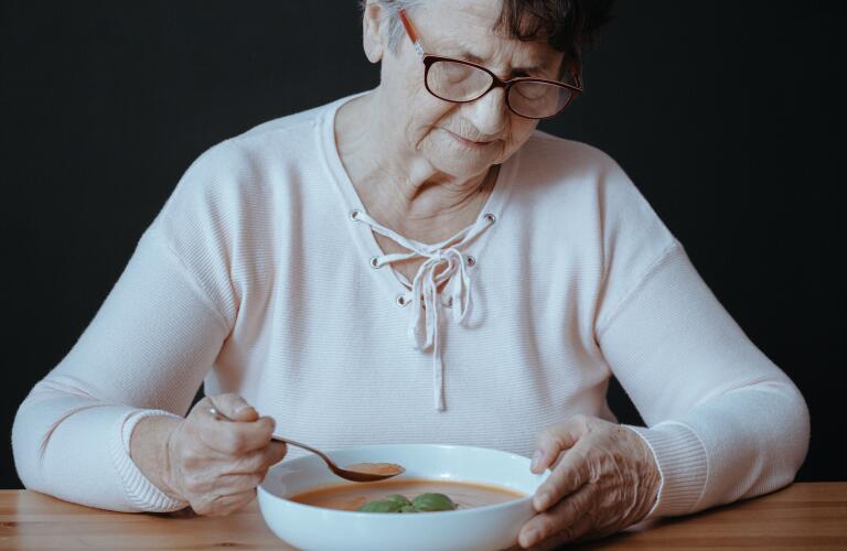 Elderly Caucasian woman with bowl of soup experiencing loss of appetite