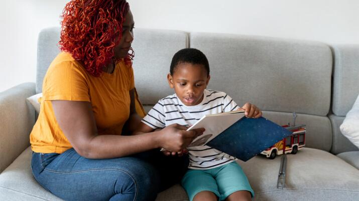 Mother and young son reading a book together on a couch