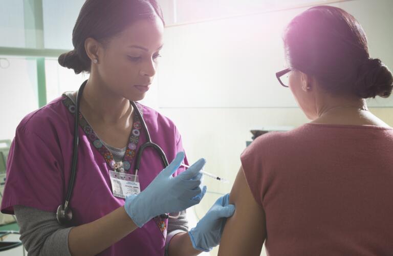 Young African American nurse or nurse practitioner giving injection or flu shot in arm of female patient