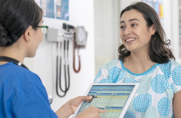 Young Hispanic woman in medical gown smiling nurse or technician holding digital tablet