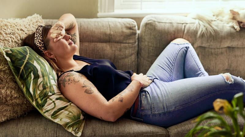 Woman lying on couch with one hand over lower abdomen and other arm over her eyes