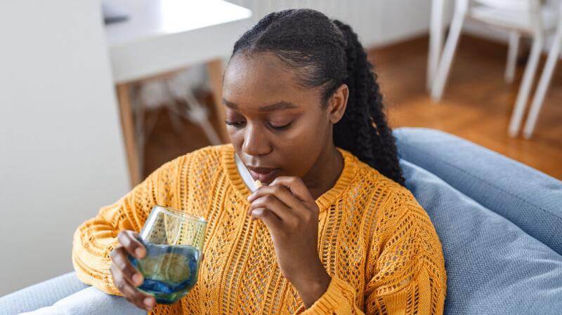 young woman on couch taking a pill with water