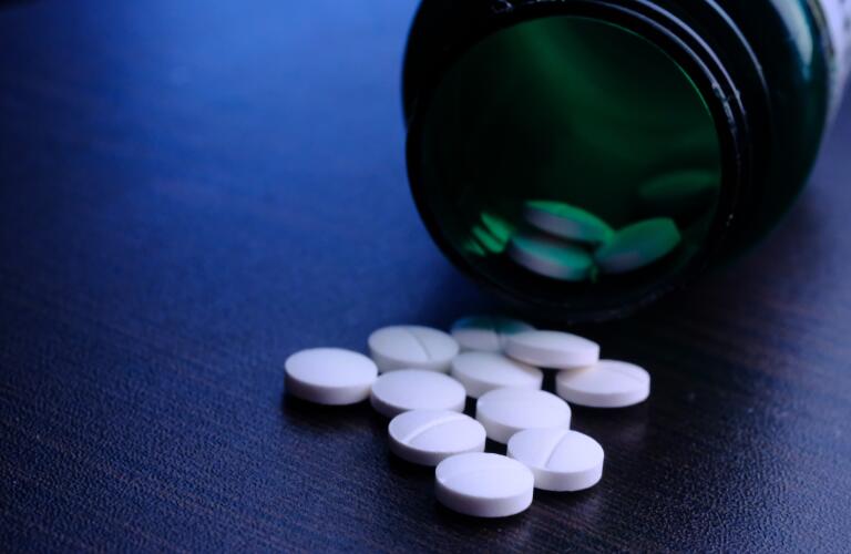 white pills spilling out of prescription bottle on table