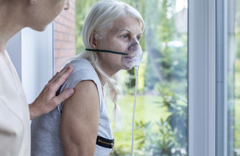 nurse supporting sick senior woman with oxygen mask and pale skin, bluish lips (cyanosis)