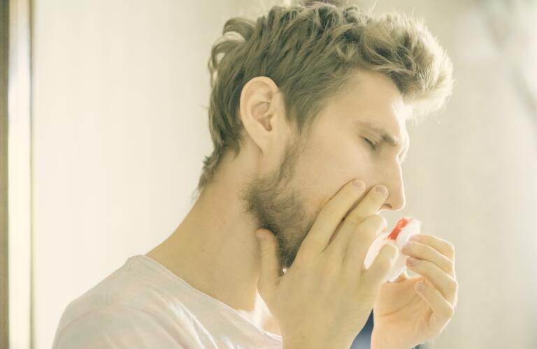 closeup bearded man with nosebleed using tissue