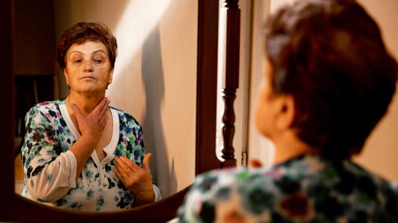 A woman looking in the mirror and touching the front of her neck