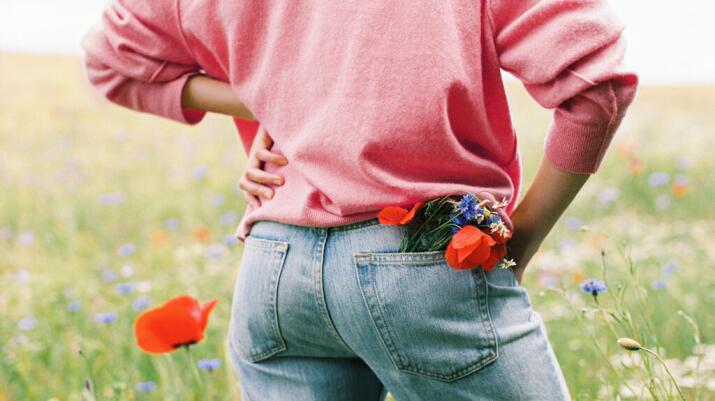 Person stands in field of flowers holding lower back and hip 