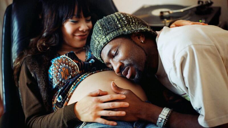 A man laying his head on a pregnant woman's stomach