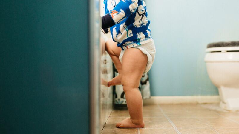 Toddler stands in bathroom wearing diaper