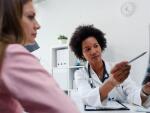 female doctor pointing to x-ray film while talking with female patient at desk in medical office