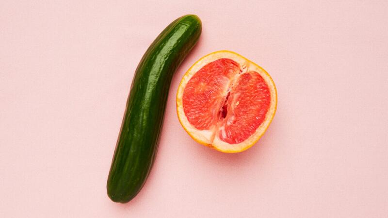 A cucumber and a grapefruit on a pink background